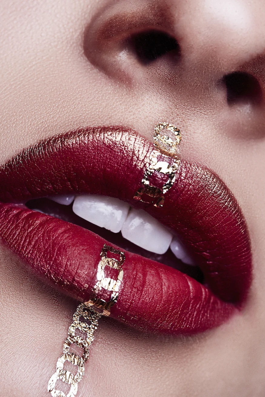 Crimson lip with gold chain detail. High-fashion editorial beauty by Bonnie Gillies